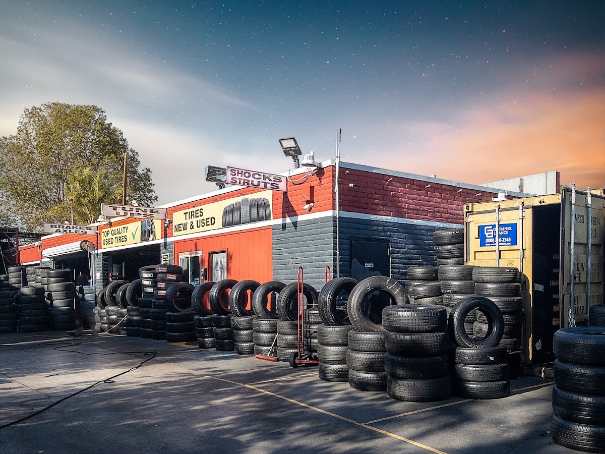 The Whittier Tires yard on Imperial Hwy at dusk, rows of tires stacked across the forecourt beneath the shop's signs
